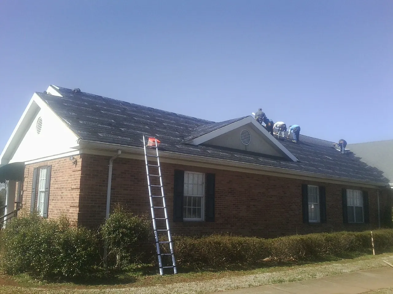 Crew tearing shingles off a brick ranch roof with a ladder set — Metal Roof Repair work by our crew in West Chicago