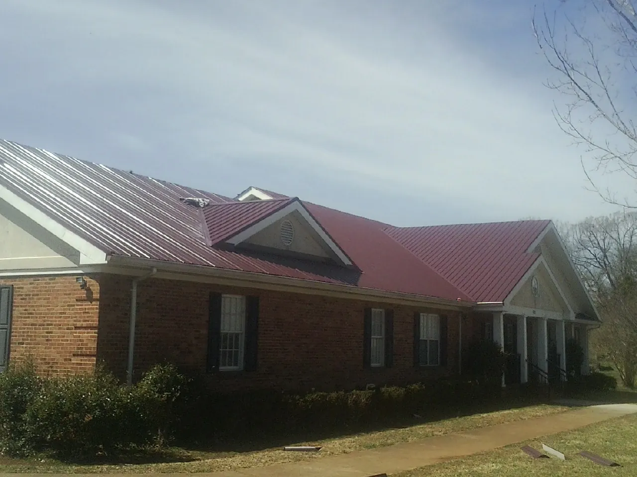 Red metal roof with gabled entries on a long brick building, from a Hail Damage Roof Repair job in West Chicago
