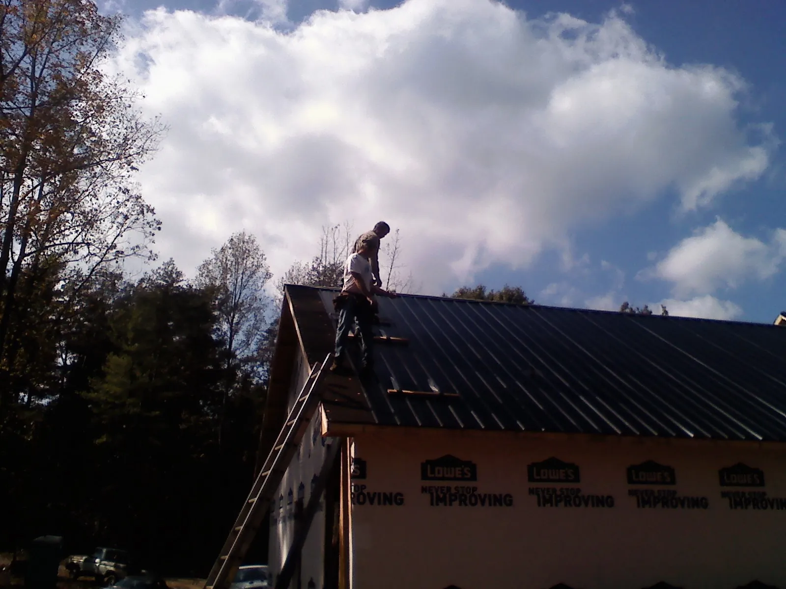 Roofer fastening dark metal panels high against a cloudy sky, from a Roof Inspection job in West Chicago