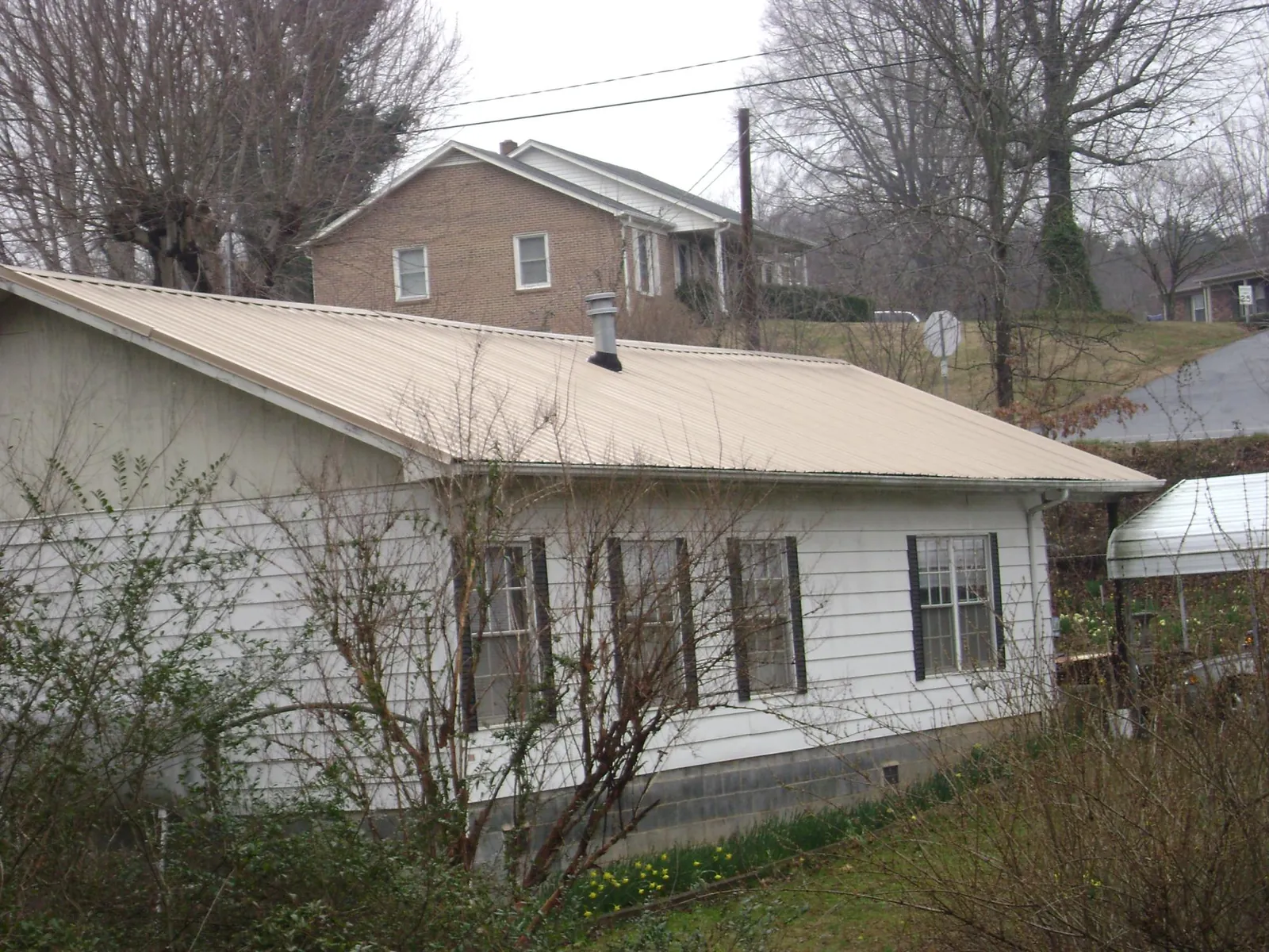 Tan metal roof on a white sided house set into a hillside — Commercial Roofing by Roofing Brothers in West Chicago